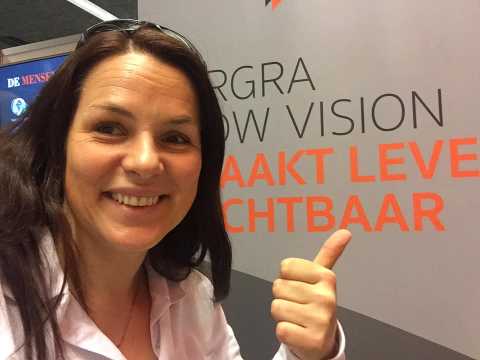 Annemiek voor een zuil van Ergra Low Vision op de ZieZobeurs